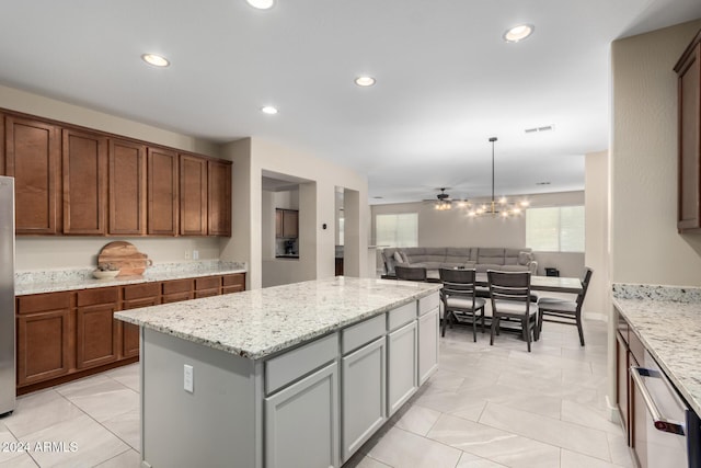 kitchen featuring pendant lighting, ceiling fan, gray cabinets, a kitchen island, and light stone counters