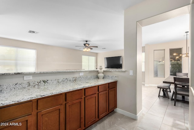 kitchen with light tile patterned floors, light stone counters, and ceiling fan