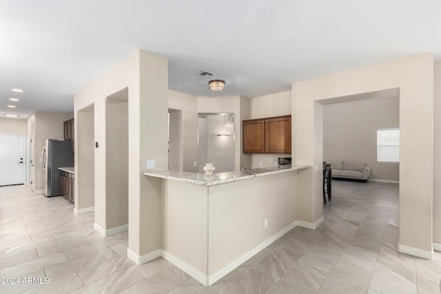 kitchen with stainless steel refrigerator, light stone countertops, and kitchen peninsula