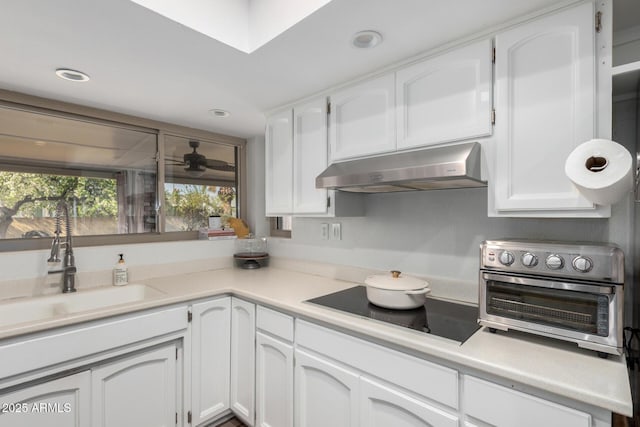 kitchen featuring black electric stovetop, light countertops, white cabinetry, a sink, and under cabinet range hood