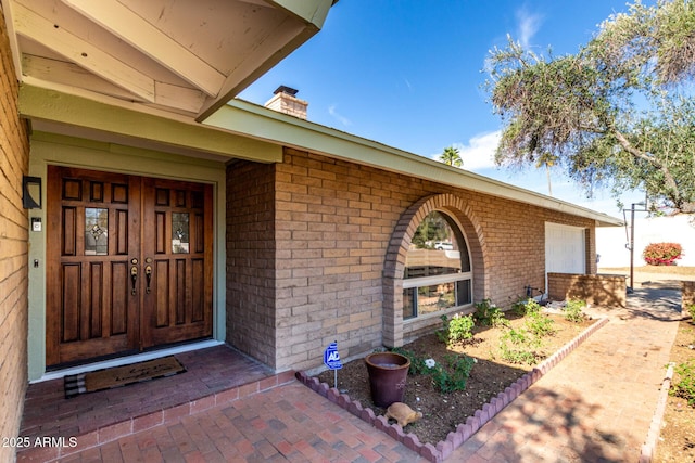 property entrance with a garage, brick siding, and a chimney