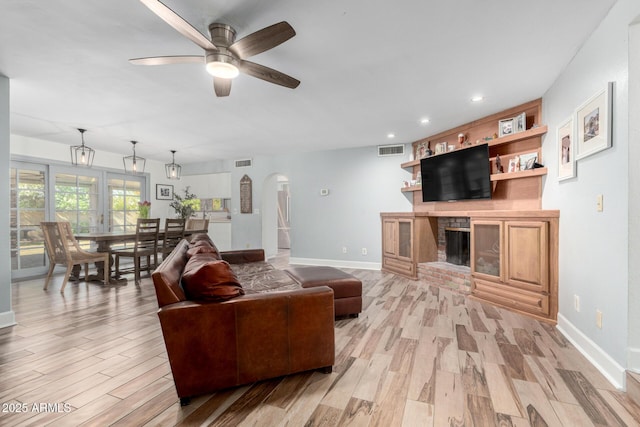 living area with arched walkways, light wood finished floors, a fireplace, and visible vents