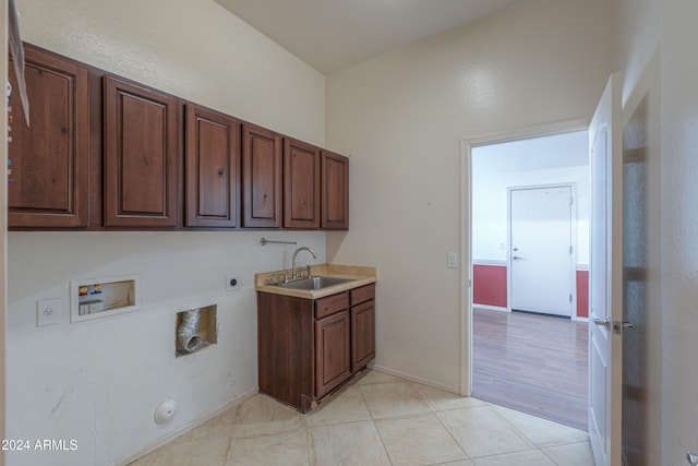 clothes washing area featuring electric dryer hookup, washer hookup, sink, light tile patterned floors, and cabinets