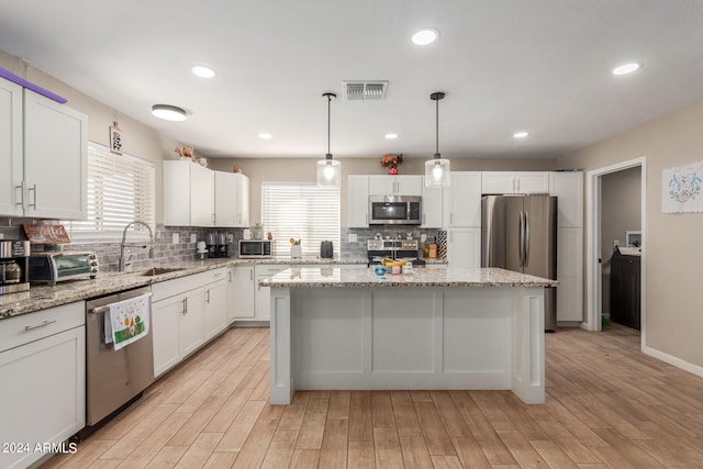 kitchen with light wood-type flooring, a wealth of natural light, a kitchen island, and appliances with stainless steel finishes