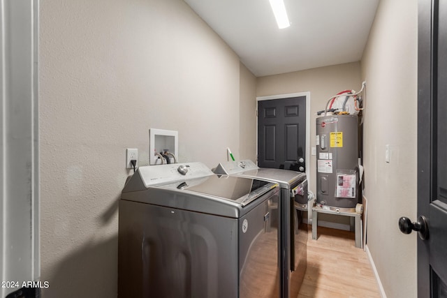 clothes washing area featuring water heater, washing machine and dryer, and light hardwood / wood-style flooring