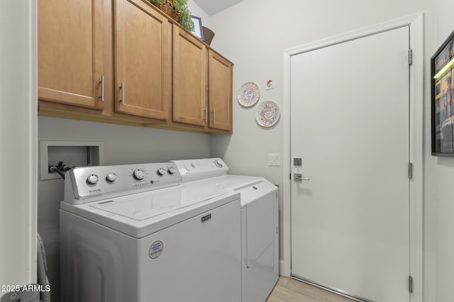 clothes washing area featuring cabinets, light hardwood / wood-style floors, and washer and dryer