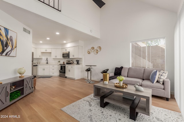 living room featuring light wood-type flooring, a high ceiling, and sink