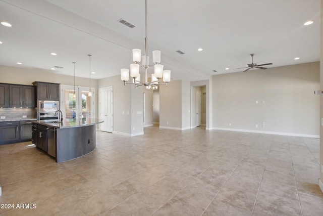 kitchen featuring light stone countertops, ceiling fan with notable chandelier, stainless steel appliances, a center island with sink, and hanging light fixtures