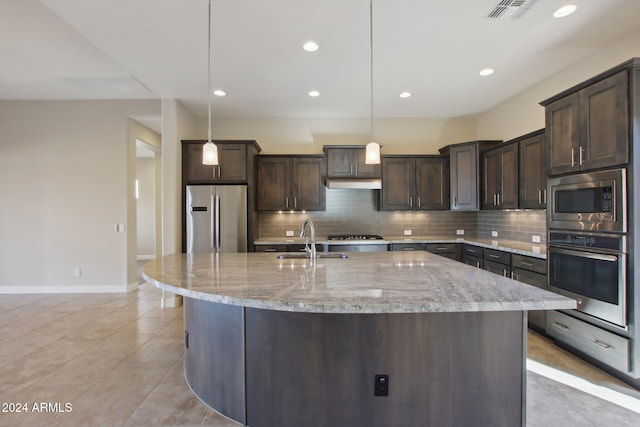 kitchen featuring appliances with stainless steel finishes, dark brown cabinetry, sink, decorative light fixtures, and a center island with sink