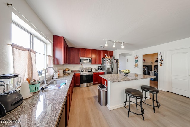 kitchen with reddish brown cabinets, a sink, washing machine and dryer, and stainless steel appliances