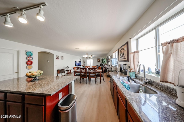 kitchen featuring an inviting chandelier, light wood-type flooring, arched walkways, a sink, and dark stone countertops