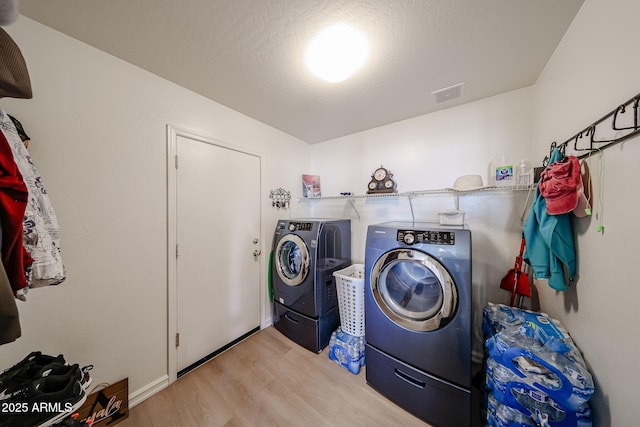 clothes washing area with visible vents, laundry area, independent washer and dryer, and wood finished floors