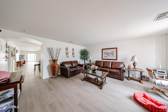 living room featuring light wood-style floors, arched walkways, baseboards, and visible vents