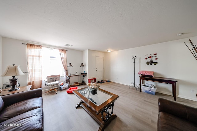 living room with baseboards, a textured ceiling, visible vents, and light wood-style flooring