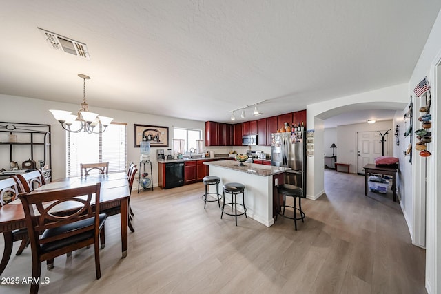 kitchen featuring dark brown cabinets, arched walkways, a kitchen breakfast bar, stainless steel appliances, and visible vents
