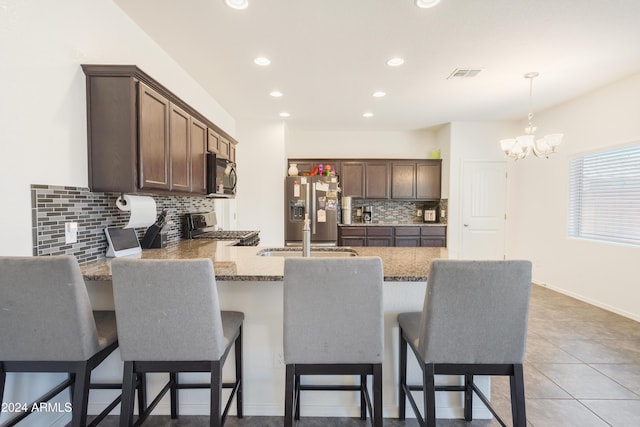 kitchen featuring appliances with stainless steel finishes, a kitchen breakfast bar, dark brown cabinetry, decorative light fixtures, and a chandelier