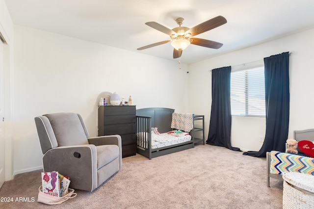 bedroom featuring ceiling fan, a crib, and light carpet