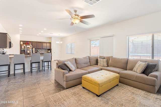 tiled living room with ceiling fan with notable chandelier