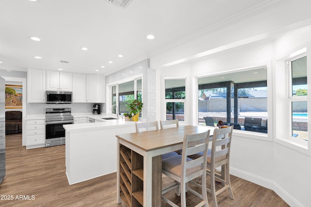 2607 E Mercer Ln, Phoenix, AZ 85028 - kitchen with stainless steel appliances, ornamental molding, white cabinets, light wood-type flooring, and a peninsula