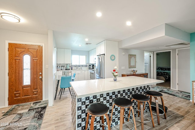 kitchen featuring stove, white cabinets, tasteful backsplash, a kitchen bar, and stainless steel fridge with ice dispenser