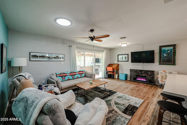 living room with a high end fireplace, wood-type flooring, ceiling fan, and brick wall