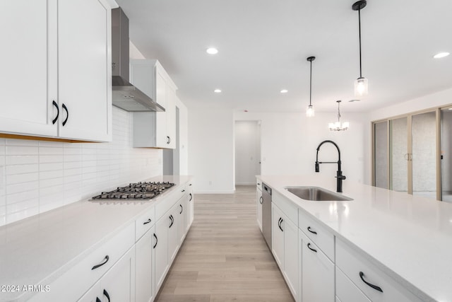 kitchen with wall chimney exhaust hood, sink, decorative light fixtures, light hardwood / wood-style flooring, and white cabinetry