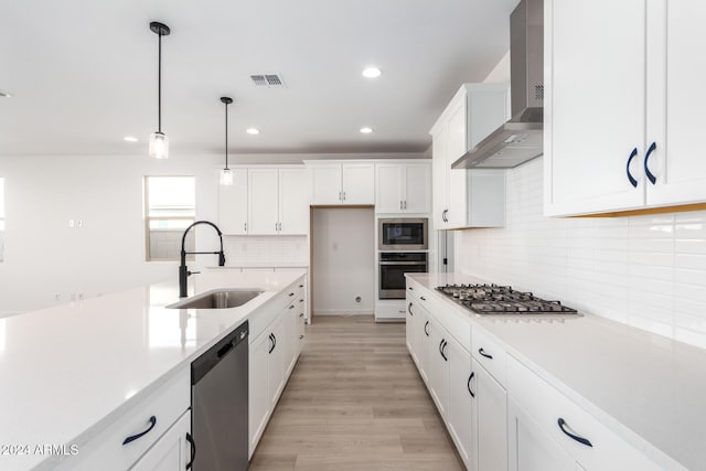 kitchen featuring light wood-type flooring, stainless steel appliances, sink, wall chimney range hood, and white cabinetry