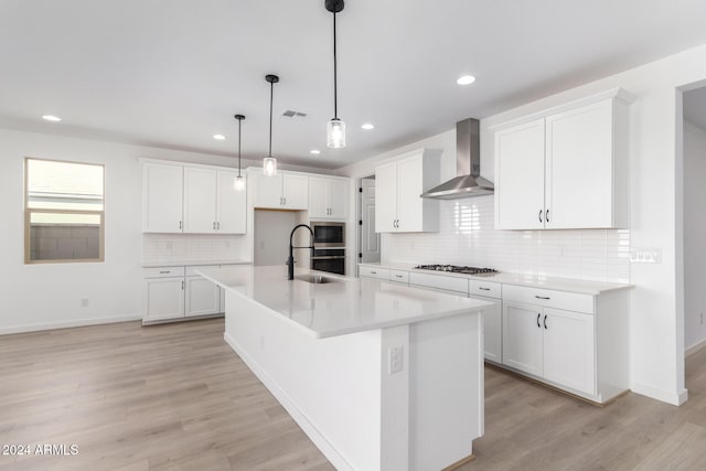 kitchen with white cabinets, appliances with stainless steel finishes, an island with sink, and wall chimney range hood