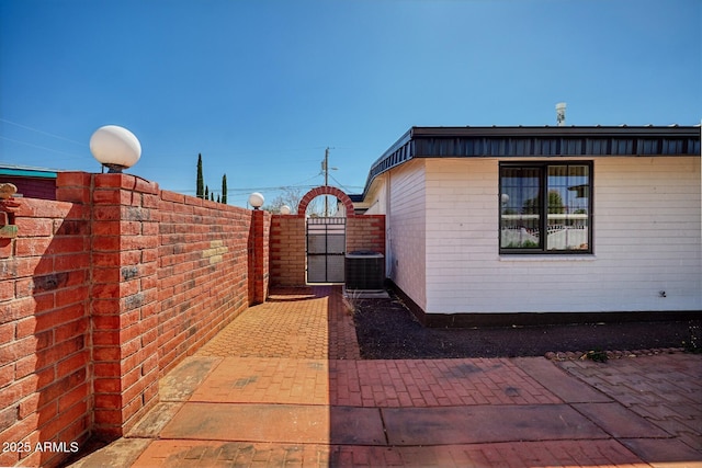 view of property exterior with central AC unit, fence, and a gate