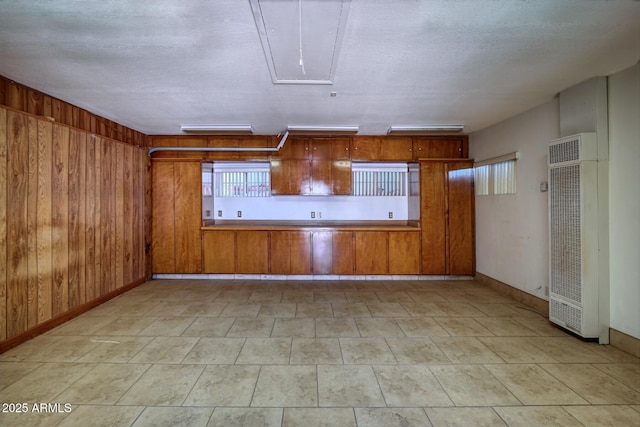 kitchen with a textured ceiling, wooden walls, brown cabinetry, baseboards, and a heating unit