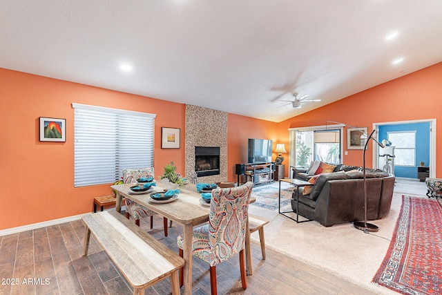 dining area with baseboards, ceiling fan, wood finished floors, vaulted ceiling, and a fireplace