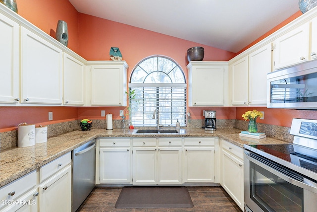 kitchen with appliances with stainless steel finishes, dark wood-type flooring, white cabinetry, vaulted ceiling, and a sink