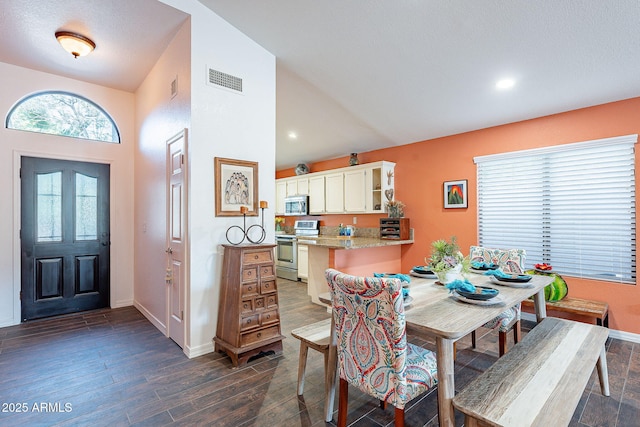 dining room featuring dark wood-style floors, lofted ceiling, visible vents, and baseboards