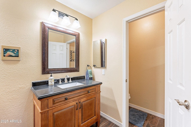 bathroom with toilet, vanity, baseboards, and wood finished floors