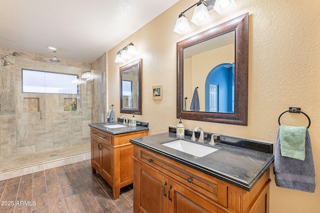 bathroom featuring a textured wall, wood finish floors, a sink, and a shower stall