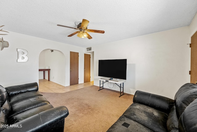 living room with a textured ceiling, ceiling fan, visible vents, arched walkways, and carpet