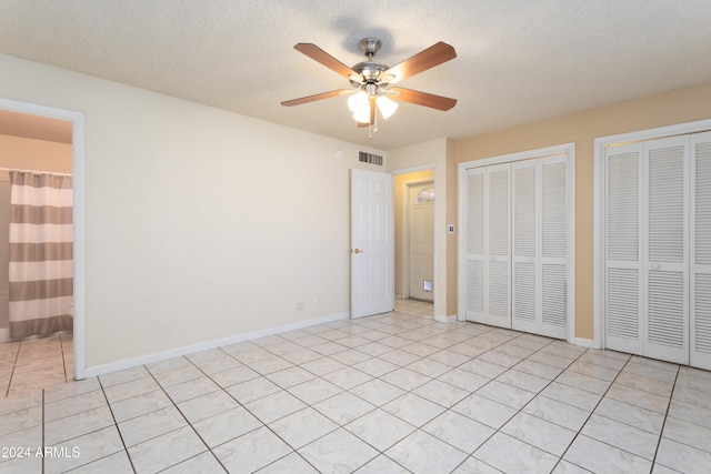 unfurnished bedroom with a textured ceiling, ensuite bath, ceiling fan, and two closets