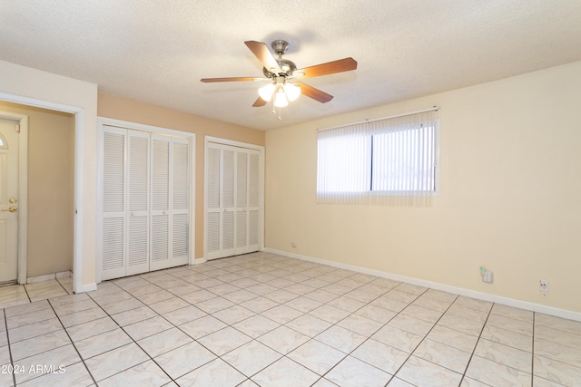 unfurnished bedroom with multiple closets, ceiling fan, light tile patterned floors, and a textured ceiling