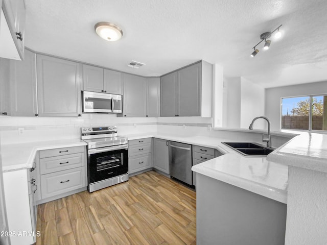 kitchen featuring sink, gray cabinetry, kitchen peninsula, stainless steel appliances, and light hardwood / wood-style floors