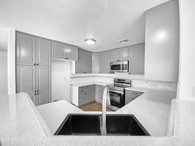 kitchen featuring appliances with stainless steel finishes, sink, a textured ceiling, and gray cabinetry