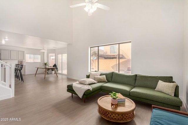 living area featuring stairway, a towering ceiling, ceiling fan, wood finished floors, and baseboards