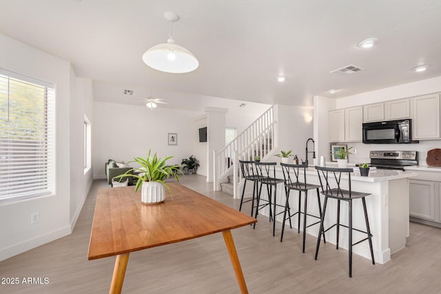 kitchen with light wood finished floors, a center island with sink, stainless steel electric range, light countertops, and black microwave