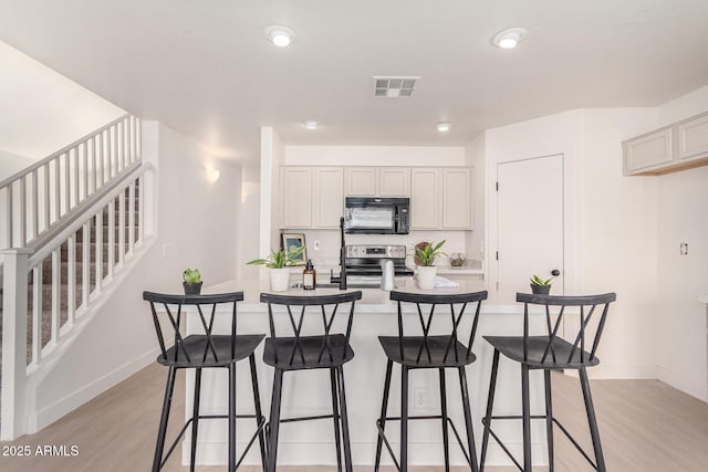 kitchen with light countertops, visible vents, light wood-style flooring, stainless steel range with electric stovetop, and black microwave