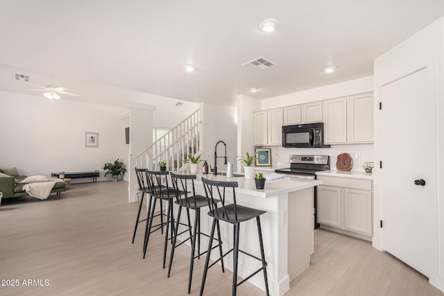 kitchen featuring a center island with sink, visible vents, light countertops, stainless steel range with electric stovetop, and black microwave