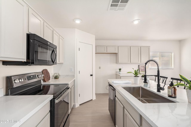 kitchen with visible vents, light wood-style flooring, light stone countertops, stainless steel appliances, and a sink