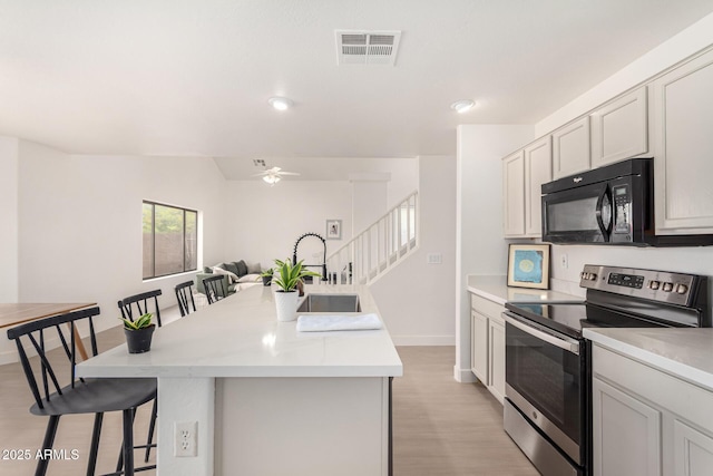 kitchen featuring electric range, black microwave, a breakfast bar, and light countertops