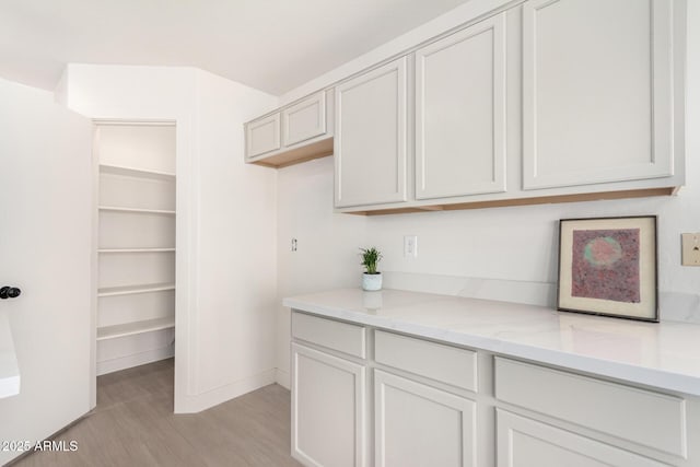 interior space featuring light stone countertops, baseboards, white cabinets, and light wood finished floors