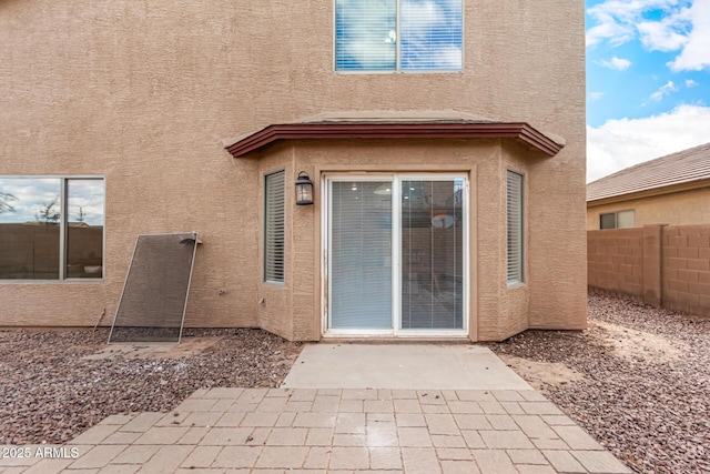 entrance to property with a patio area, fence, and stucco siding