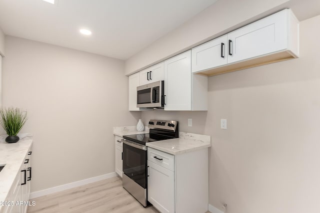 kitchen with light stone counters, light wood-style floors, white cabinets, baseboards, and appliances with stainless steel finishes