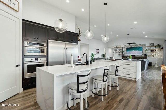 kitchen with sink, decorative light fixtures, appliances with stainless steel finishes, dark hardwood / wood-style floors, and a kitchen island with sink